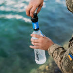 Військовий під’єднує фільтр Sawyer Squeeze до м’якої пляшки Sawyer біля водойми